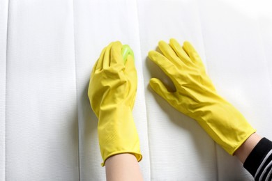 Photo of Woman in yellow gloves cleaning white mattress with brush, top view