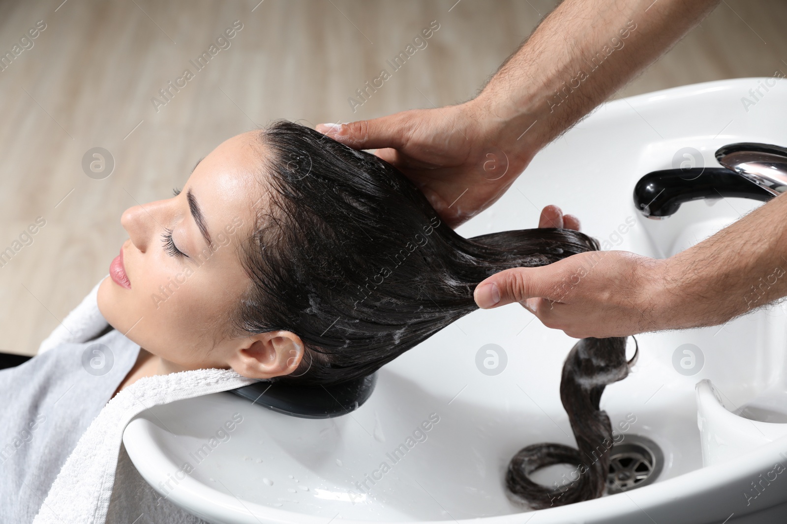 Photo of Stylist washing client's hair at sink in beauty salon