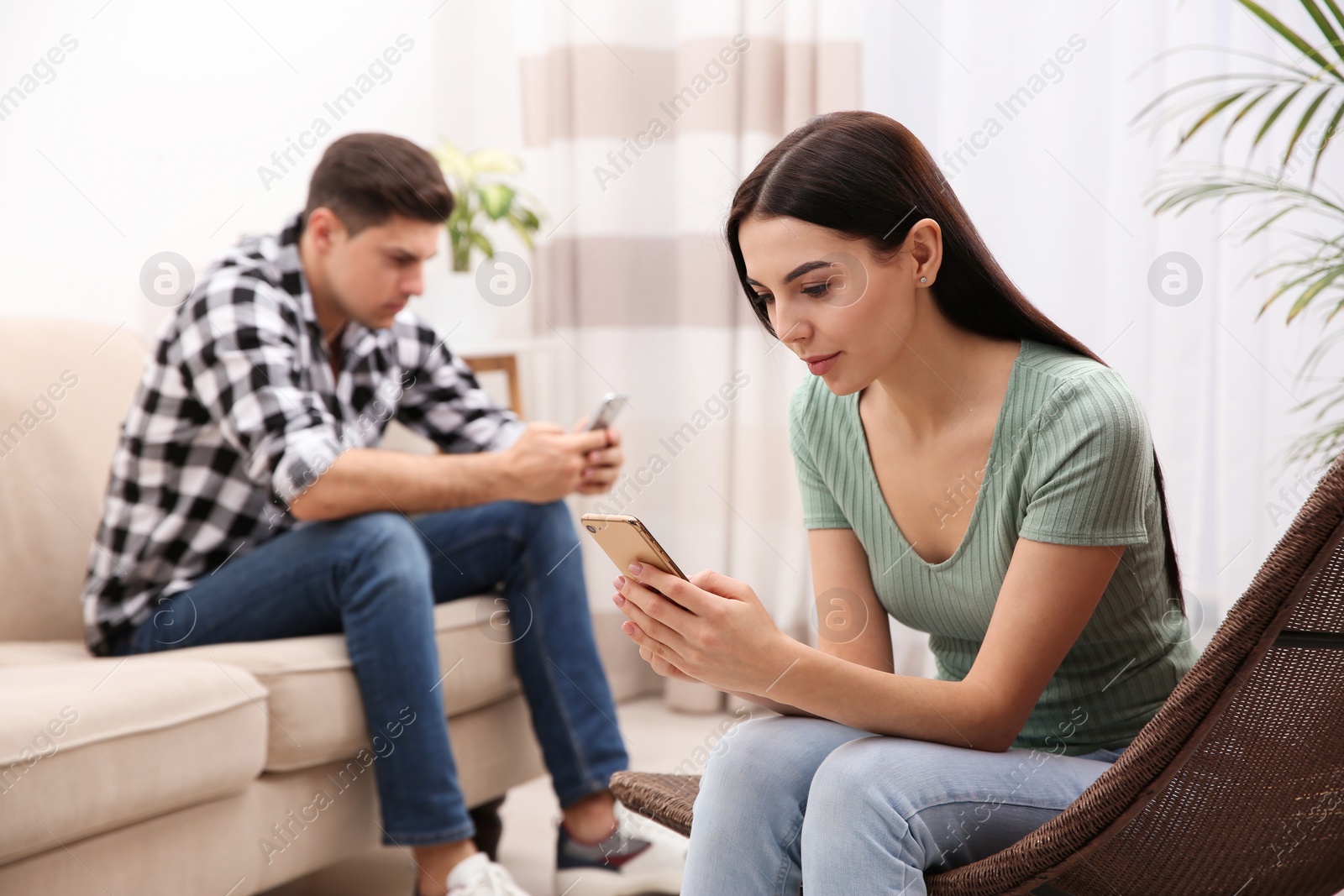 Photo of Couple addicted to smartphones ignoring each other at home. Relationship problems