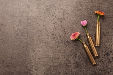 Photo of Beautiful flowers in bullet cases on grey textured table, flat lay. Space for text