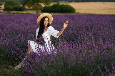 Photo of Beautiful young woman with bouquet sitting in lavender field