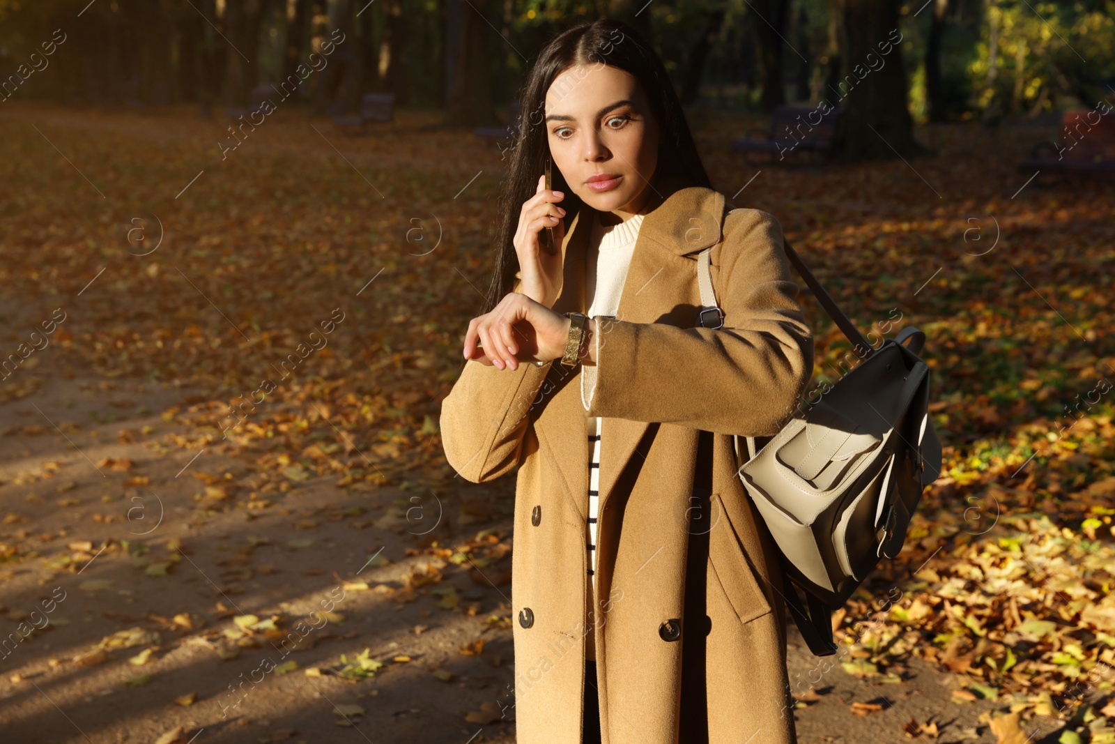 Photo of Woman checking time while talking on smartphone in park. Being late concept