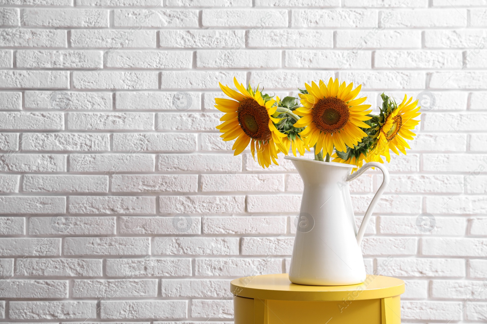 Photo of Bouquet of beautiful sunflowers on table near white brick wall. Space for text