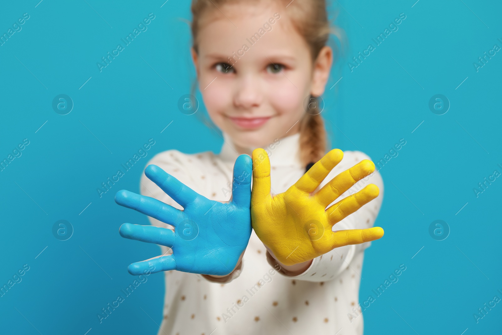 Photo of Little girl with hands painted in Ukrainian flag colors against light blue background, focus on palms. Love Ukraine concept