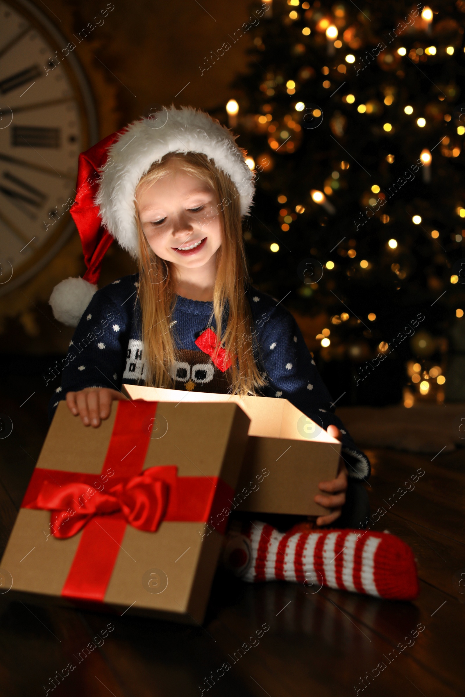 Photo of Cute child opening magic gift box near Christmas tree at night