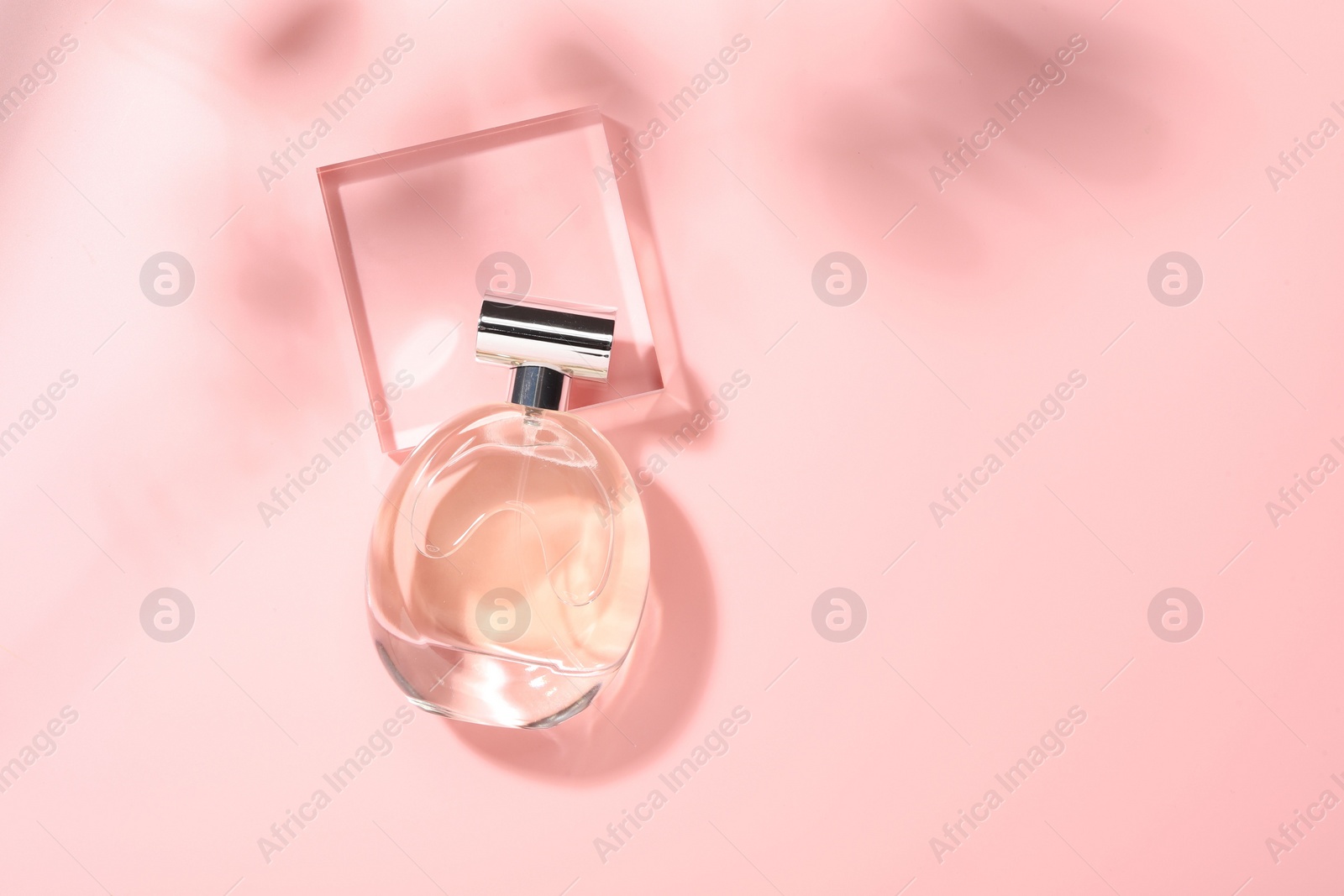 Photo of Bottle of luxury women's perfume in sunlight on pink background, top view. Space for text