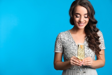 Photo of Beautiful young woman in elegant dress holding glass of champagne on blue background, space for text. Christmas party