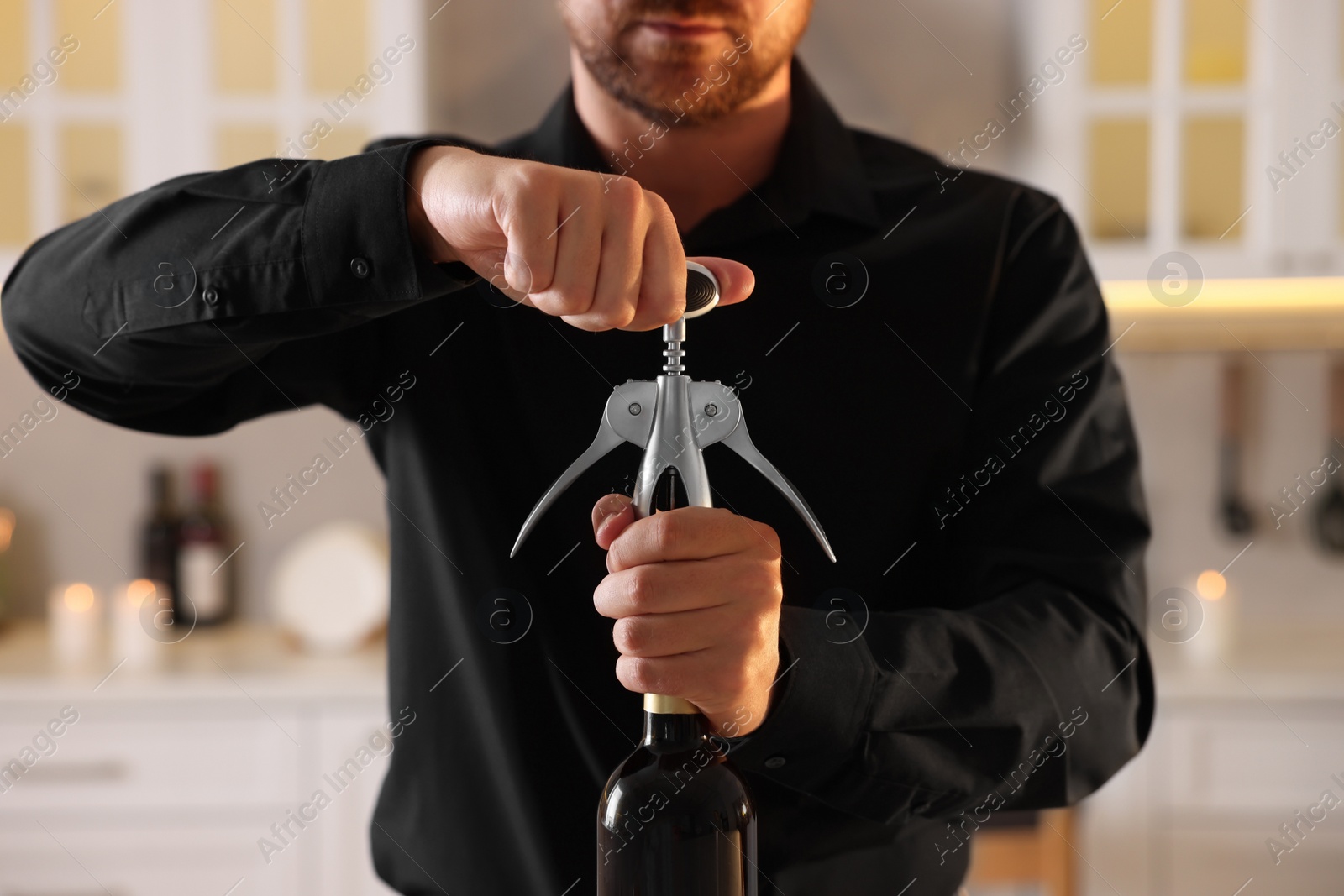 Photo of Man opening wine bottle with corkscrew in kitchen, closeup