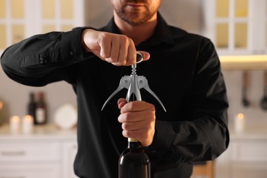 Man opening wine bottle with corkscrew in kitchen, closeup