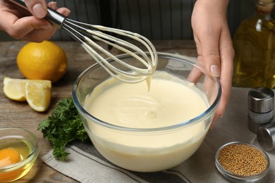 Photo of Woman making homemade mayonnaise in glass bowl at wooden table, closeup