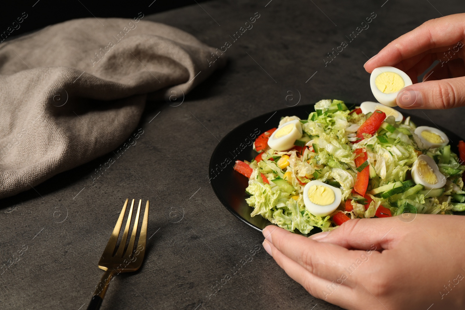 Photo of Woman making delicious salad with Chinese cabbage and quail eggs at black table, closeup