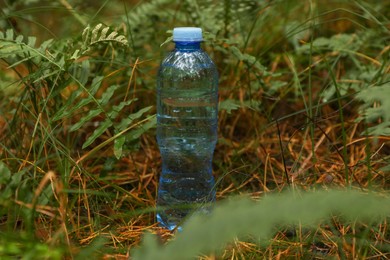 Plastic bottle of fresh water on ground in forest