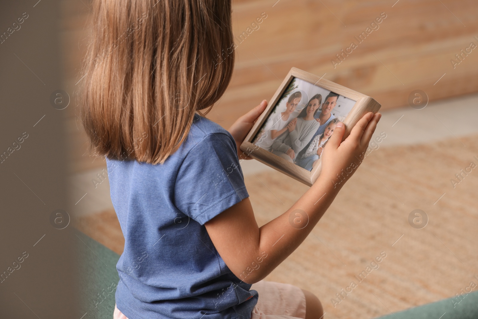 Photo of Little girl holding framed family photo indoors, closeup