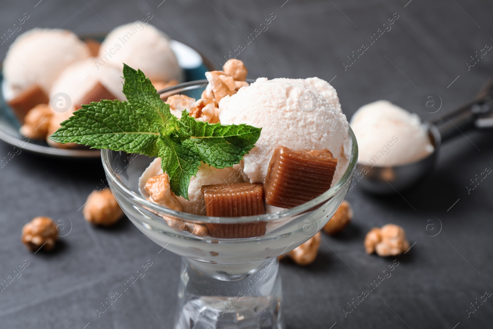 Photo of Glass bowl of ice cream with caramel candies, popcorn and mint on grey table, closeup