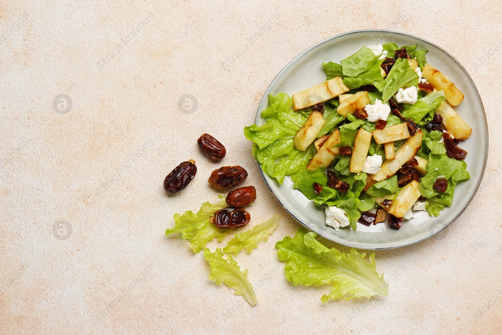 Photo of Delicious parsnip with lettuce, feta cheese and dates on beige table, flat lay. Space for text