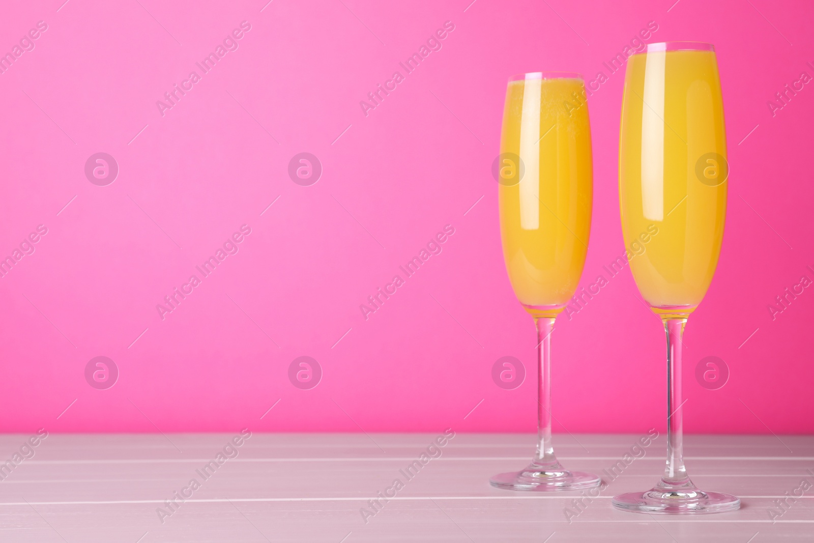 Photo of Fresh alcoholic Mimosa cocktails on wooden table against pink background, space for text