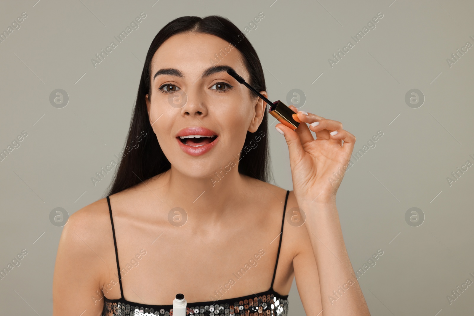 Photo of Beautiful young woman applying mascara on grey background