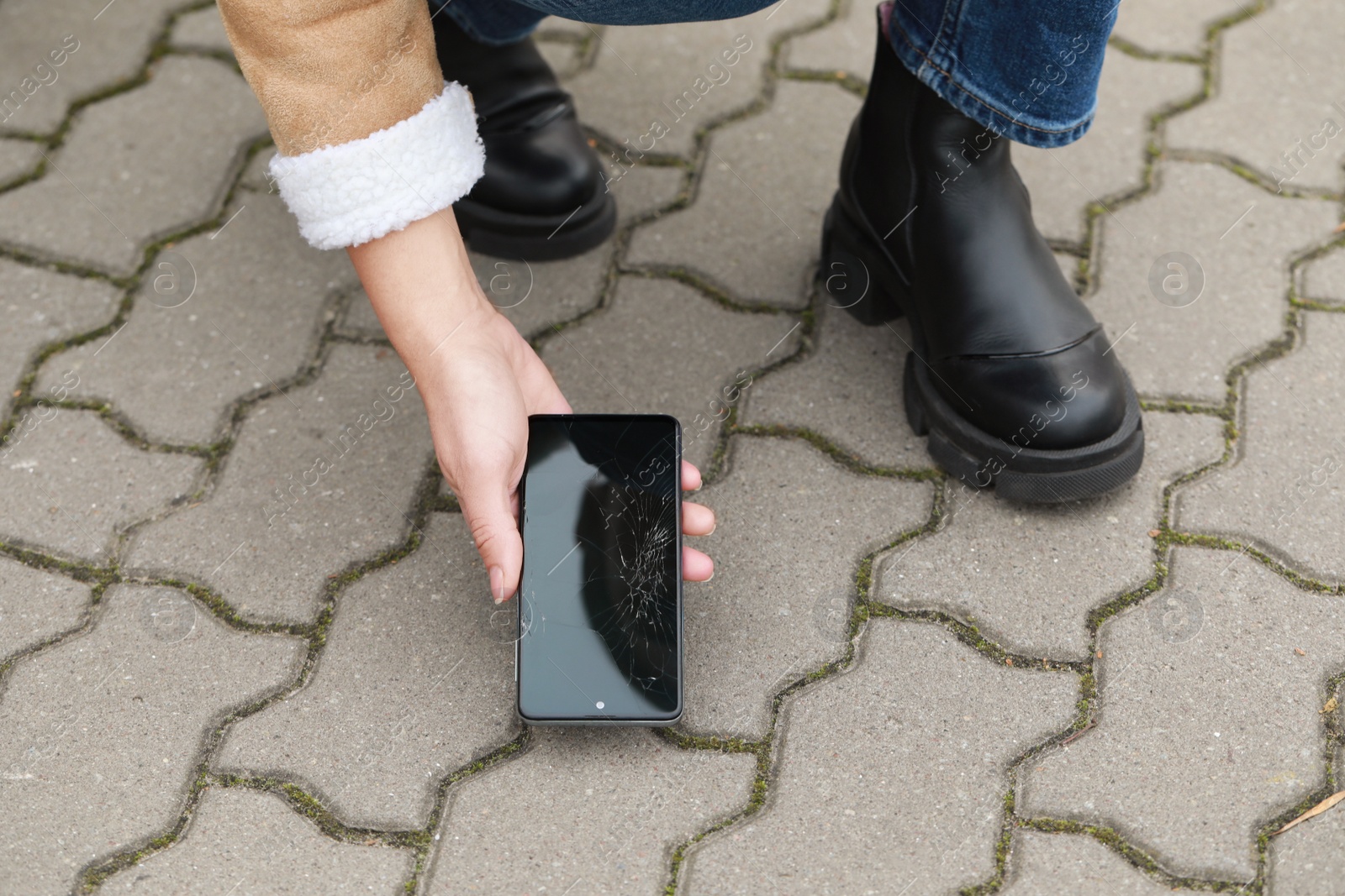 Photo of Woman taking dropped smartphone from pavement, closeup. Device repairing