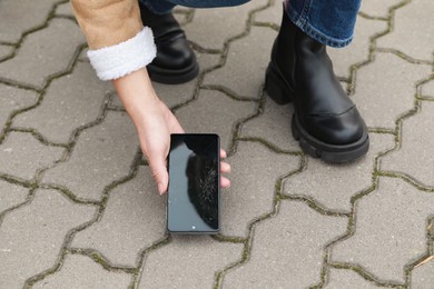 Photo of Woman taking dropped smartphone from pavement, closeup. Device repairing