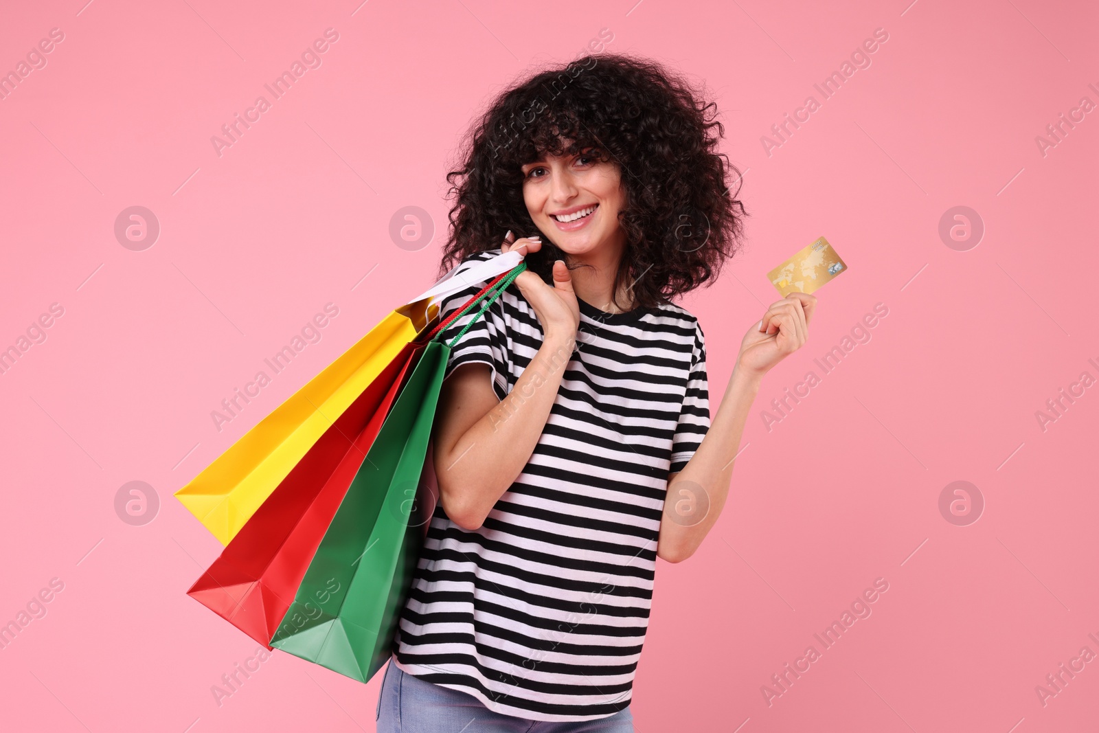 Photo of Happy young woman with shopping bags and credit card on pink background