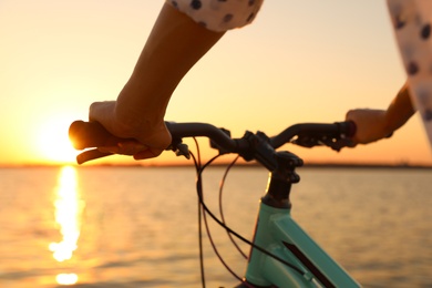 Photo of Woman riding bicycle near river at sunset, closeup