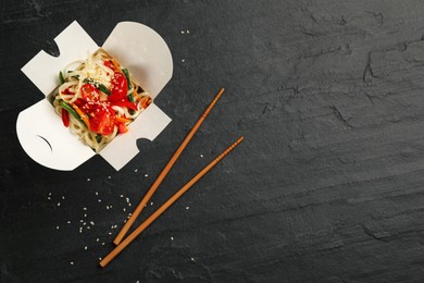 Photo of Box of vegetarian wok noodles with chopsticks on slate table, flat lay. Space for text