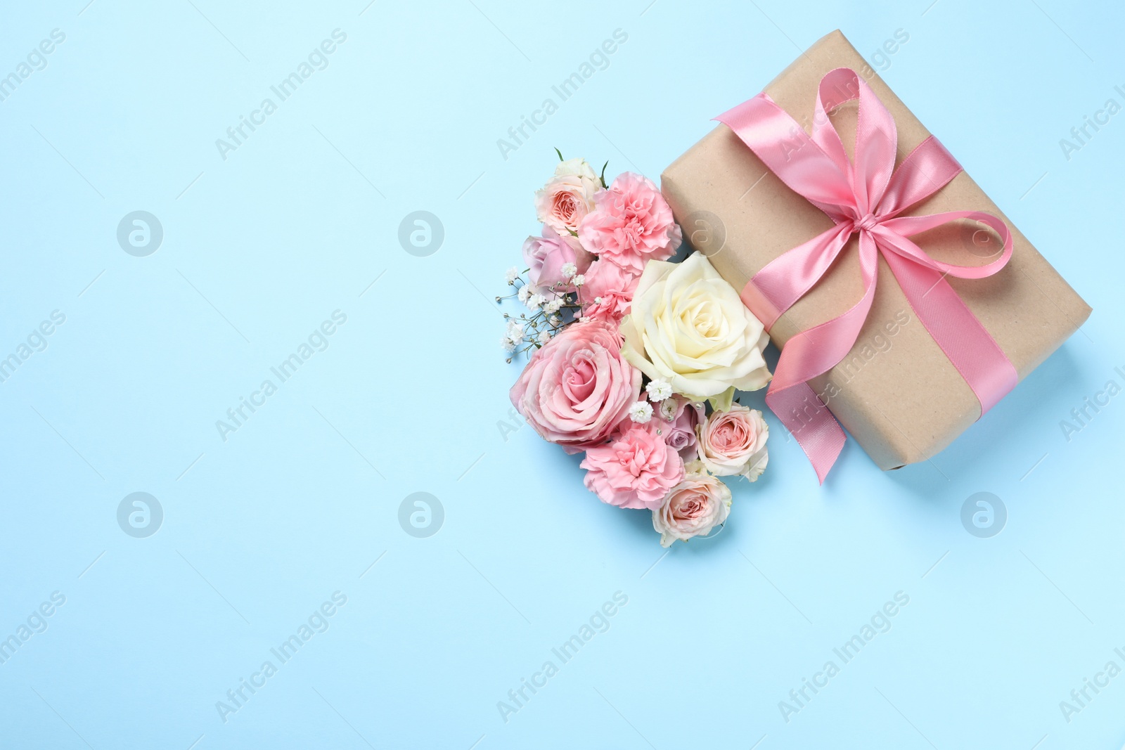 Photo of Gift box and beautiful flowers on light blue background, flat lay. Space for text