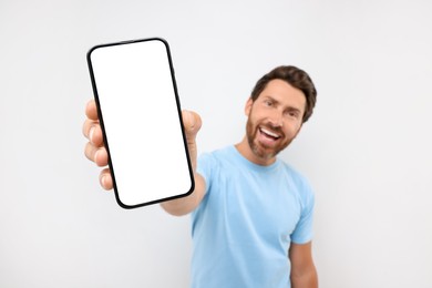 Photo of Handsome man showing smartphone in hand on white background, selective focus. Mockup for design