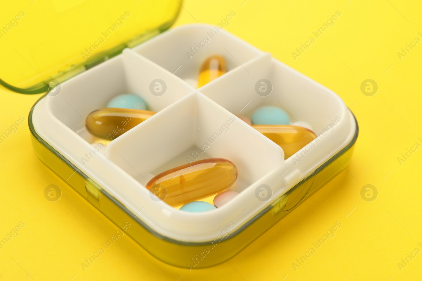 Photo of Plastic box with different pills on yellow background, closeup