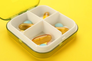 Plastic box with different pills on yellow background, closeup