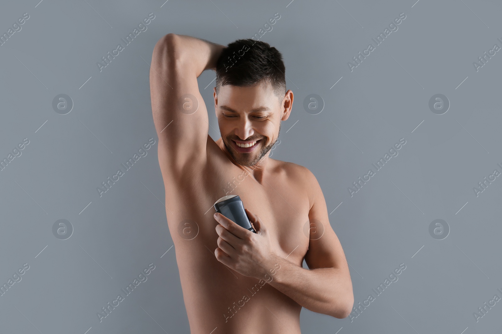 Photo of Handsome man applying deodorant on grey background