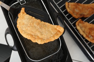 Photo of Spatula with delicious fried chebureki over deep fryer, top view