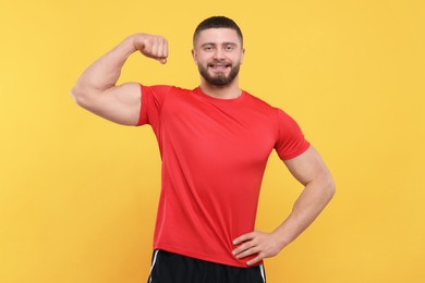 Photo of Portraithandsome man showing muscles on yellow background