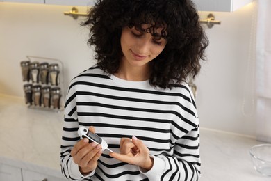 Photo of Diabetes. Woman checking blood sugar level with glucometer in kitchen