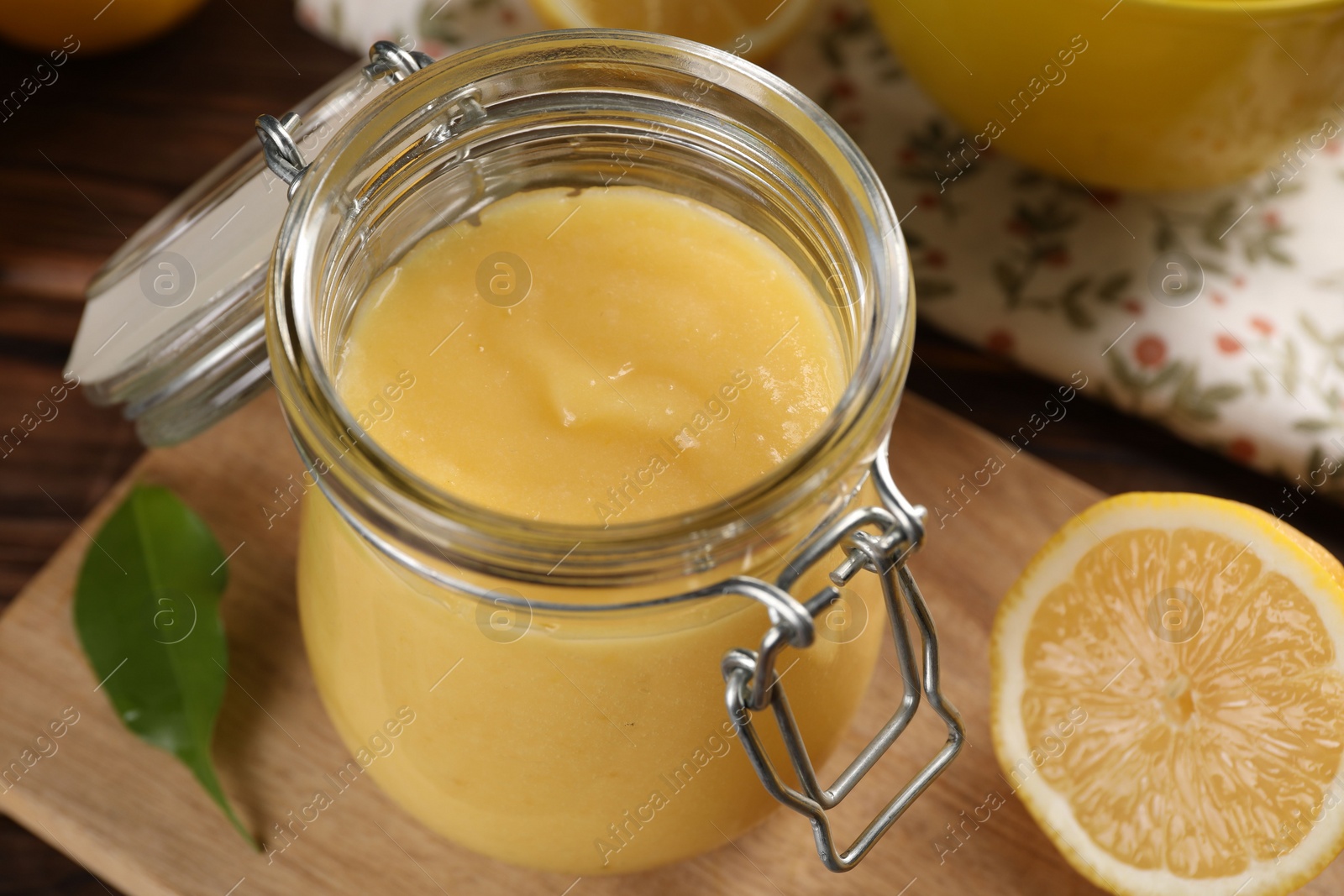 Photo of Delicious lemon curd in glass jars, fresh citrus fruit and green leaf on table, closeup