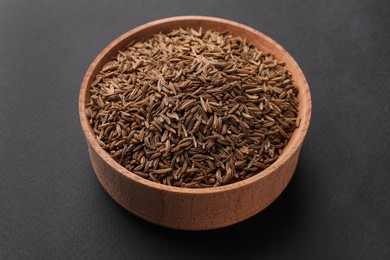 Photo of Wooden bowl with cumin seeds on grey background
