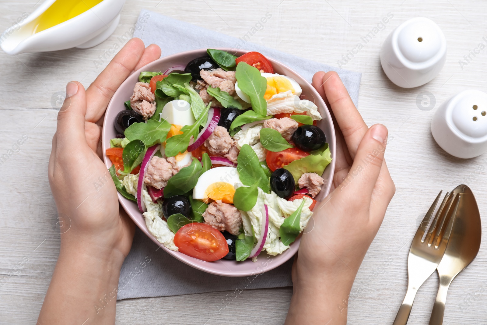 Photo of Woman holding bowl of delicious salad with canned tuna at white wooden table, top view