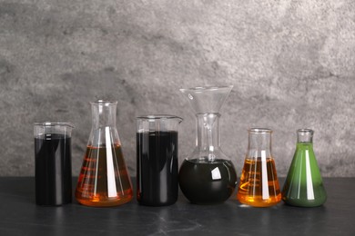 Beakers and flasks with different types of oil on grey textured table, space for text