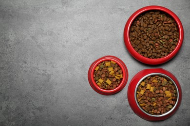 Photo of Pet bowls with dry food on grey background, flat lay. Space for text