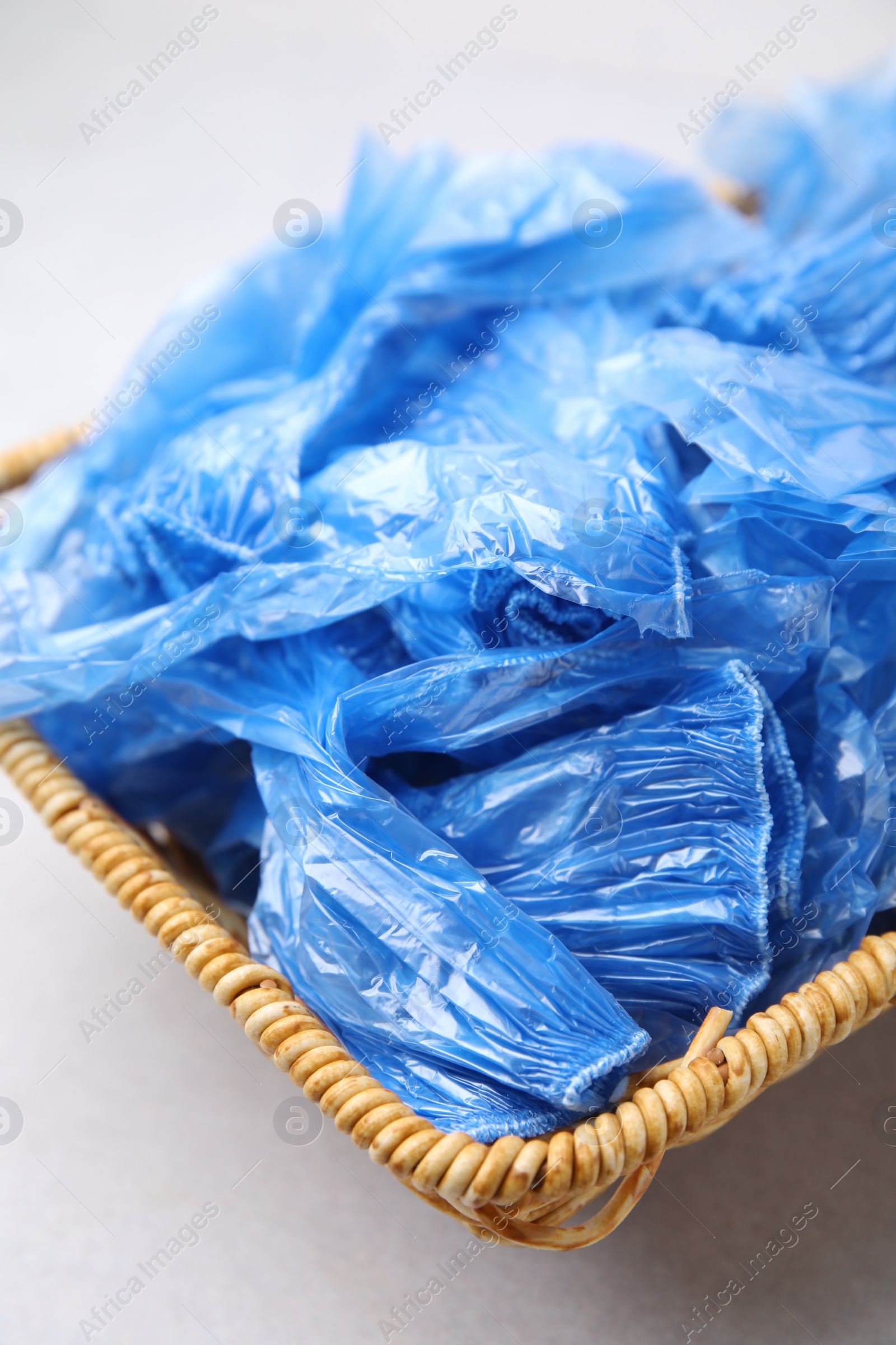 Photo of Blue medical shoe covers in wicker basket on light background, closeup