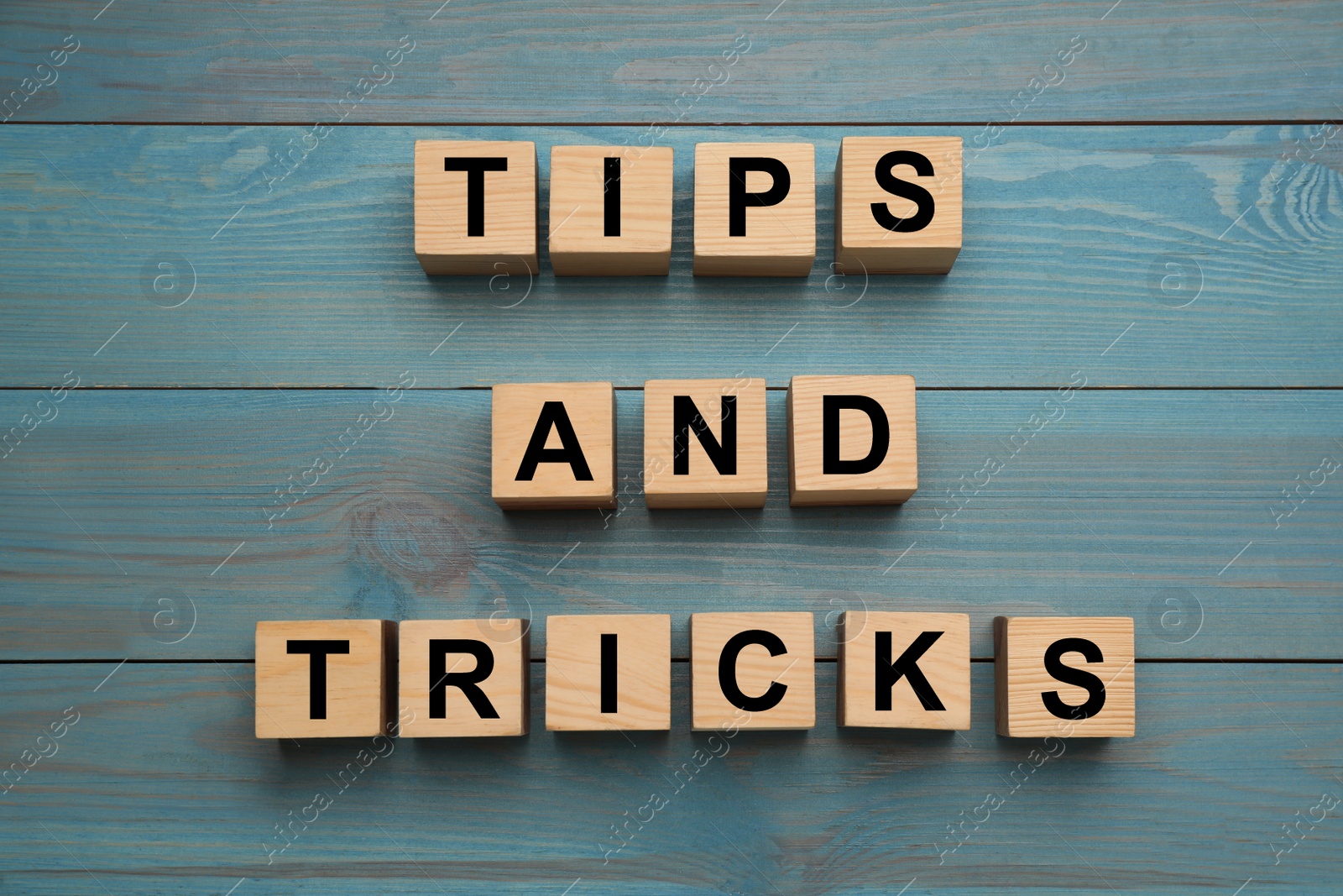 Photo of Phrase Tips and Tricks made with wooden cubes on light blue table, flat lay