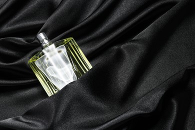 Photo of Luxury men's perfume in bottle on black satin fabric, top view. Space for text