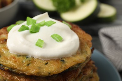 Delicious zucchini pancakes with sour cream and green onion on plate, closeup