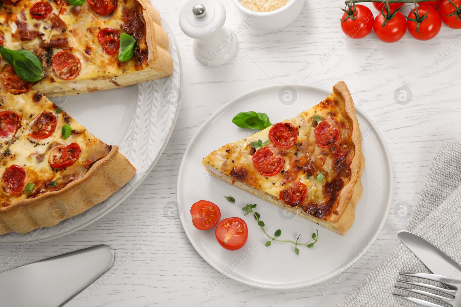 Photo of Cut delicious homemade quiche with prosciutto, tomatoes and basil on white wooden table, above view