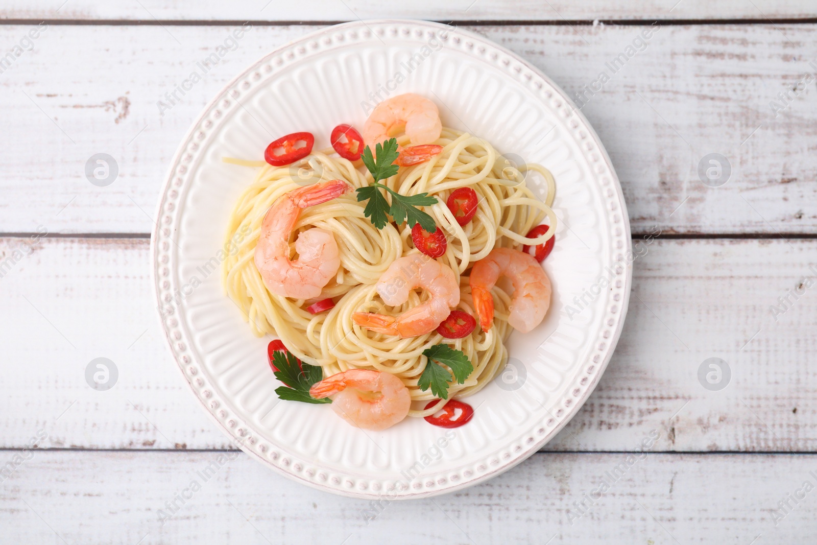 Photo of Tasty spaghetti with shrimps, chili pepper and parsley on wooden rustic table, top view