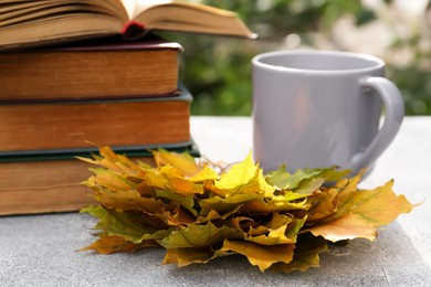 Photo of Yellow maple leaves, books and cup of tea on light gray table, closeup. Autumn atmosphere