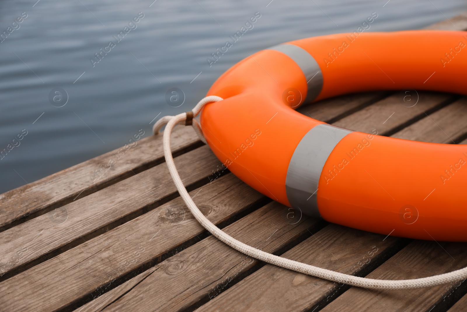 Photo of Orange lifebuoy on wooden pier near water. Rescue equipment