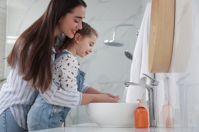 Photo of Mother and daughter washing hands with liquid soap together in bathroom
