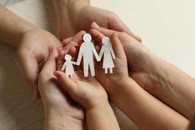 Parents and child holding paper cutout of family at white wooden table, closeup