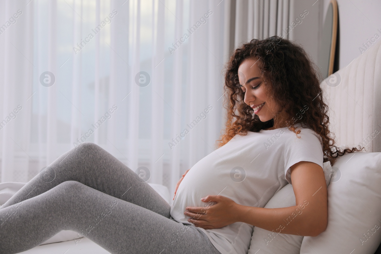 Photo of Pregnant young African-American woman sitting on bed at home